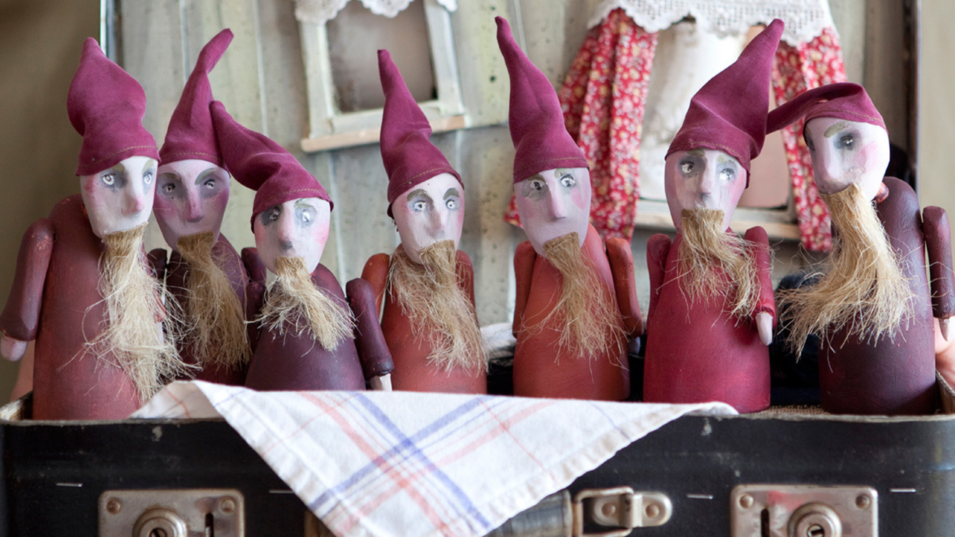 Sieben Figuren mit roten Zipfelmützen und langen Bärten, die die 7 Zwerge darstellen, stehen in einem Koffer.